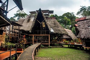 A traditional wooden structure with a thatched roof, surrounded by potted plants and a paved walkway.