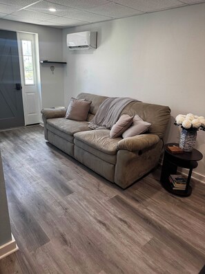 Ein Wohnzimmer mit einem beigen Sofa, einem kleinen Beistelltisch und einer Vase mit Blumen.