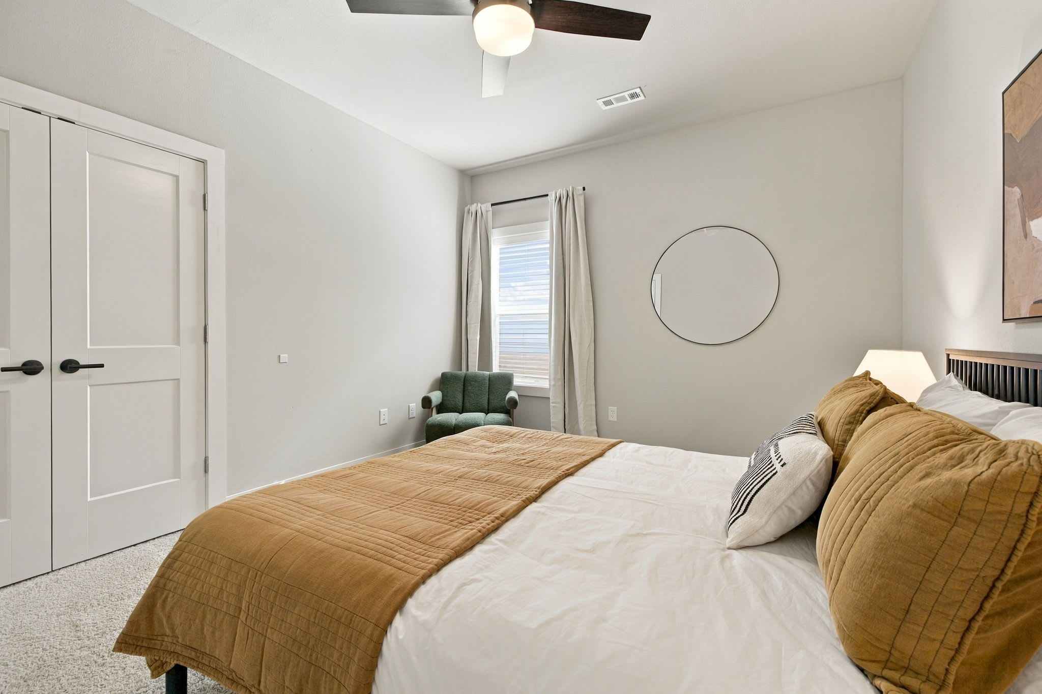 A bedroom with a bed, a chair, a round mirror, and a ceiling fan.