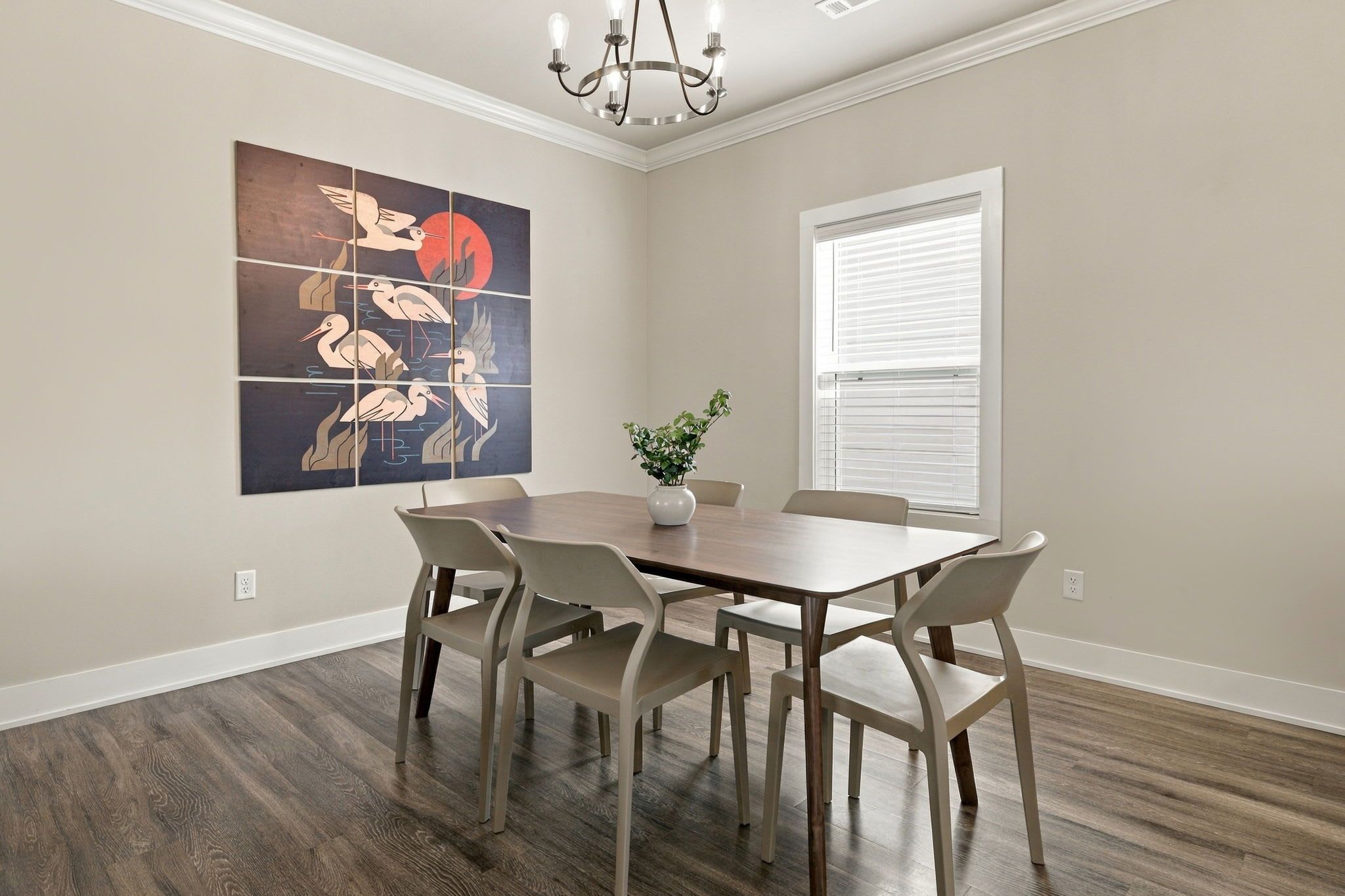 A dining area with a wooden table and chairs, a vase with a plant, and a wall-mounted artwork.