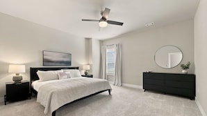 A bedroom with a bed, bedside tables, a dresser, a ceiling fan, a window with curtains, and a wall-mounted mirror. - Bear's Den - 2.3 mi to DT-Direct MTB Trail Access (Bentonville)
