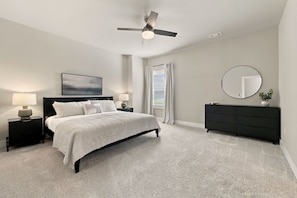 A bedroom with a bed, bedside tables, a dresser, a ceiling fan, a window with curtains, and a wall-mounted mirror. - Bear's Den - 2.3 mi to DT-Direct MTB Trail Access (Bentonville)