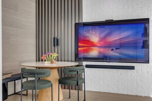Une pièce moderne avec une table ronde, deux chaises, un téléviseur fixé au mur et un mur en briques blanches.