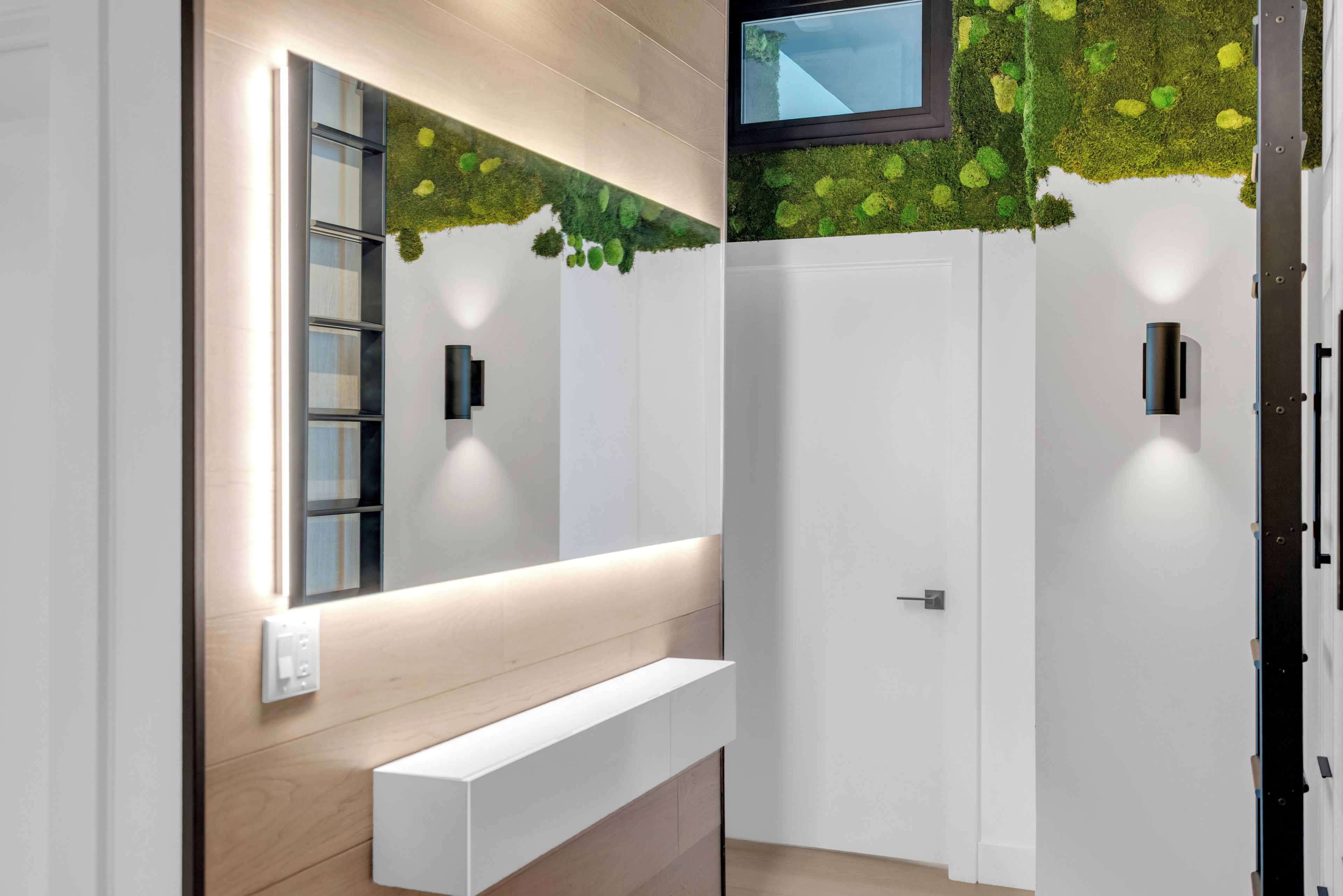 Une salle de bain moderne avec un grand miroir, un banc intégré et un luminaire fixé au mur.