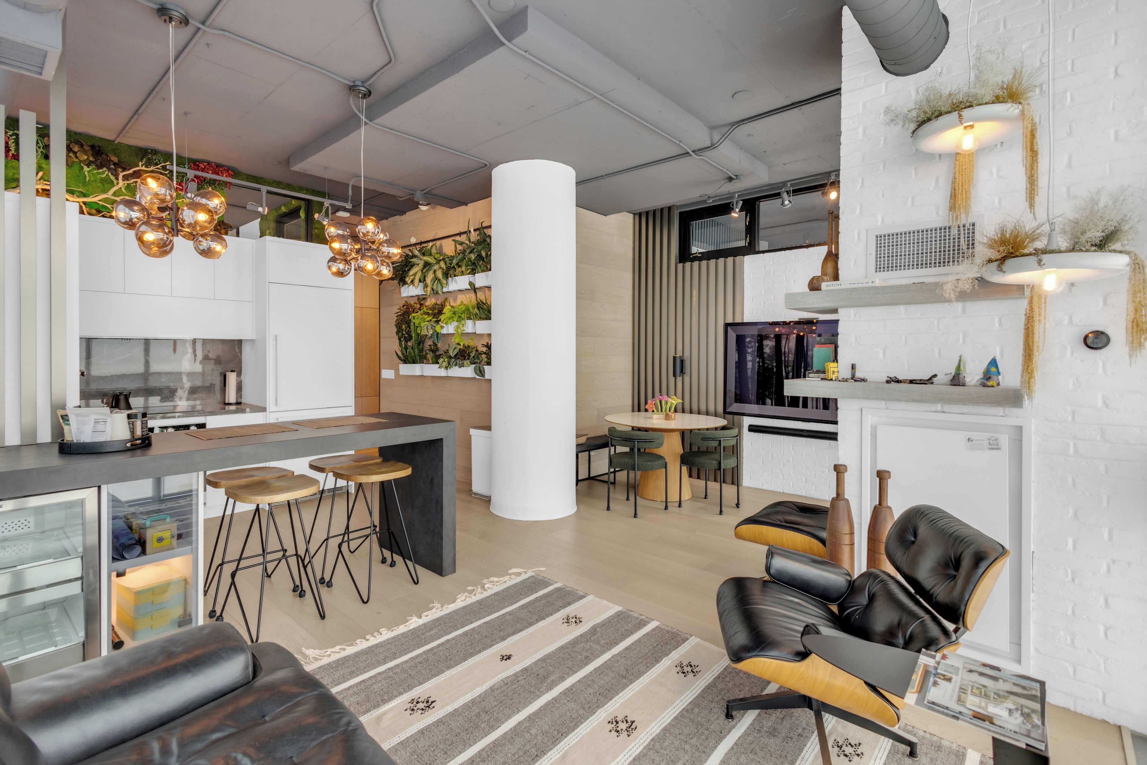 Une cuisine moderne avec des tabourets de bar, un coin repas avec une table ronde et un espace de vie avec des fauteuils en cuir.