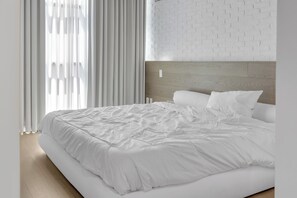 Une chambre moderne avec un grand lit, du linge de lit blanc et un mur décoré d’un motif en briques.