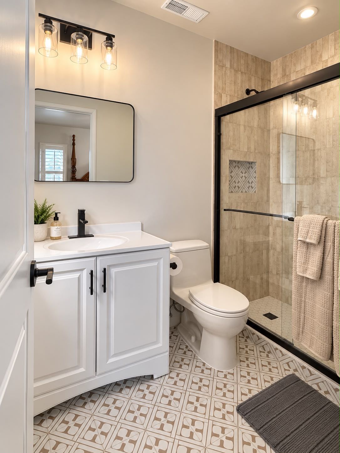 A modern bathroom with a white vanity, a toilet, a glass shower enclosure, and patterned floor tiles.