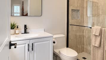 A modern bathroom with a white vanity, a toilet, a glass shower enclosure, and patterned floor tiles.