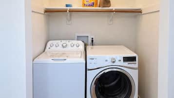 A laundry room with a washing machine and dryer, wooden flooring, and a shelf with laundry supplies.