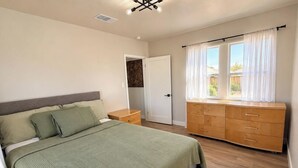 A bedroom with a bed, a dresser, a nightstand, and a window with curtains.