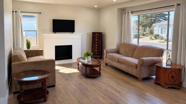 A living room with a fireplace, two sofas, a coffee table, and a TV mounted on the wall.
