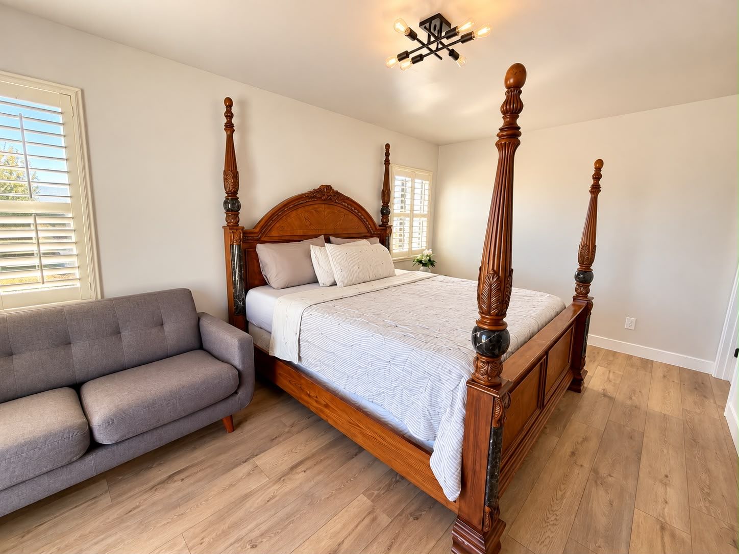 Ein Bett mit Baldachin, ein hölzernes Kopfteil, ein graues Sofa und ein Holzboden.