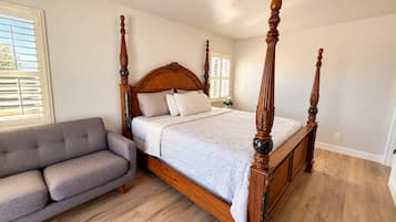 Ein Bett mit Baldachin, ein hölzernes Kopfteil, ein graues Sofa und ein Holzboden.
