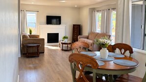 A spacious living area with a fireplace, a television mounted above it, and a dining table set with chairs.