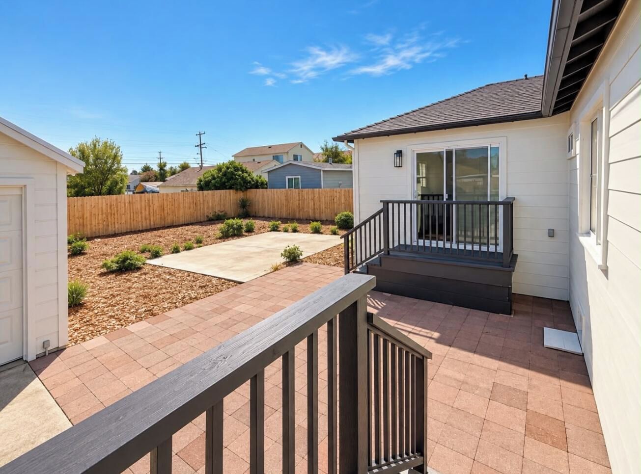 A residential backyard with a wooden deck, a concrete patio, and a small staircase leading to a covered area.