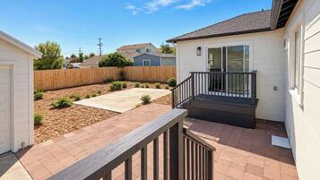 A residential backyard with a wooden deck, a concrete patio, and a small staircase leading to a covered area.