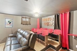 Een bioscoopzaal in huis met een leren bank, rode bioscoopstoelen en een bord met daarop 'filmavond'.
