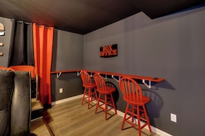 Een kamer met een bar, twee rode barkrukken, een zwart gordijn en een bordje met de tekst 'BOX OFFICE'.