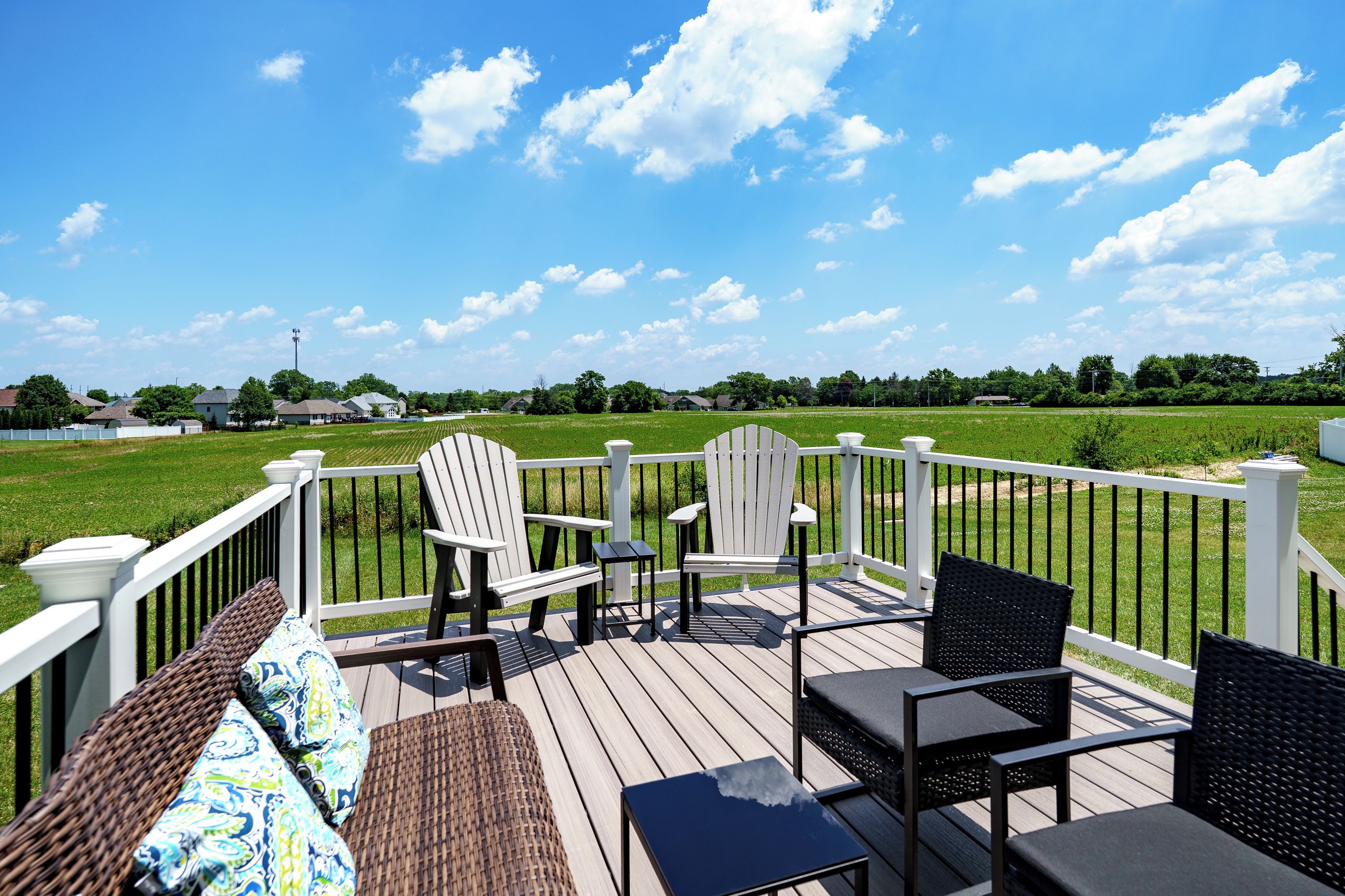 A deck with outdoor furniture, a view of a green field, and a clear sky.