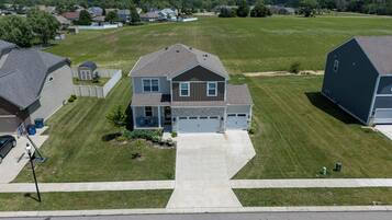 A residential area with a two-story house featuring a front porch, garage, and a well-maintained lawn.