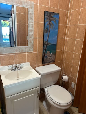 Une salle de bain avec un lavabo blanc, des toilettes et un tableau représentant une scène de plage au mur.