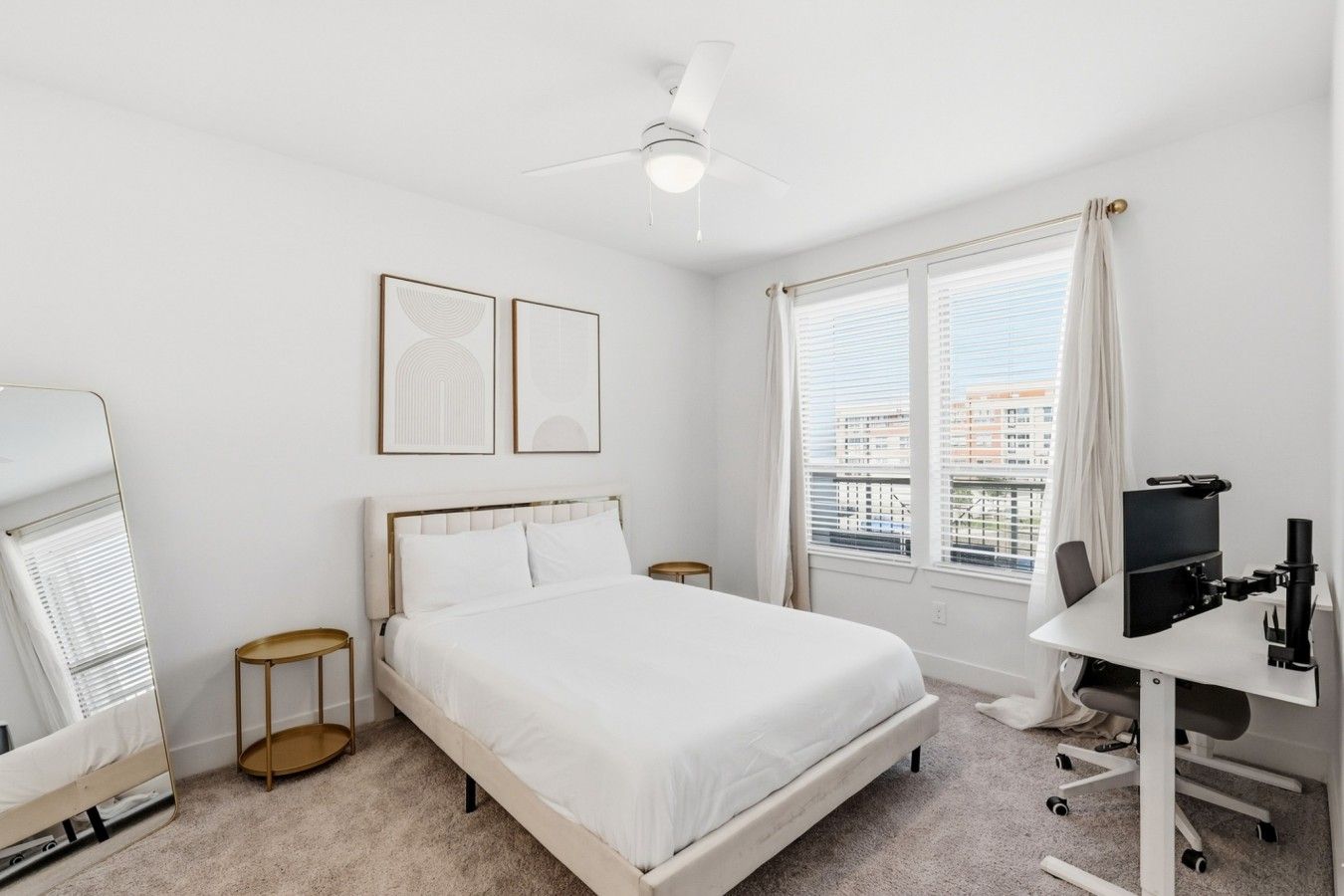 Una camera d'albergo con un letto, una scrivania con un computer, una ventola a soffitto e una finestra con persiane.