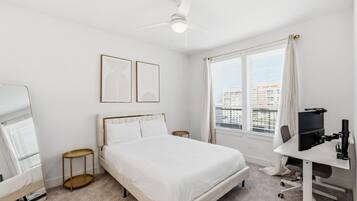 Una camera d'albergo con un letto, una scrivania con un computer, una ventola a soffitto e una finestra con persiane.