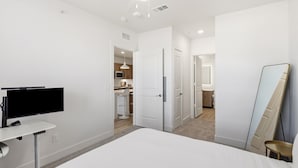 A bedroom with a bed, a TV, a mirror, and a door leading to a bathroom. - Modern 1BR Apartment near PGA and Universal Studios (Frisco)