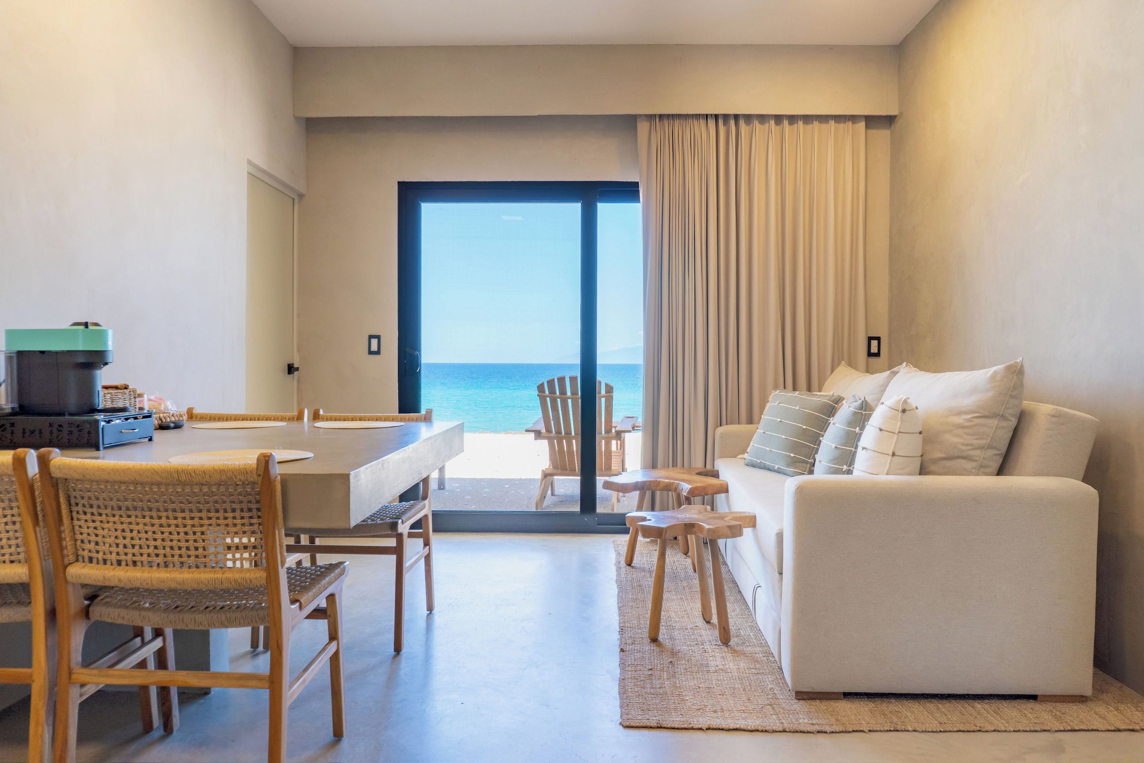 Un salón moderno con vista al mar, un comedor con mesa y sillas, y un sofá con cojines.