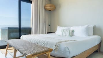 A hotel room with a large bed, a bench, a woven light fixture, and a view through a large window.