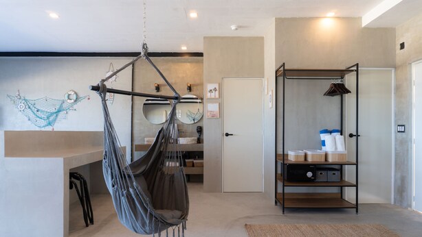 Une pièce avec un fauteuil suspendu, une étagère en bois avec des boîtes de rangement, une porte et un mur décoré de différents objets.