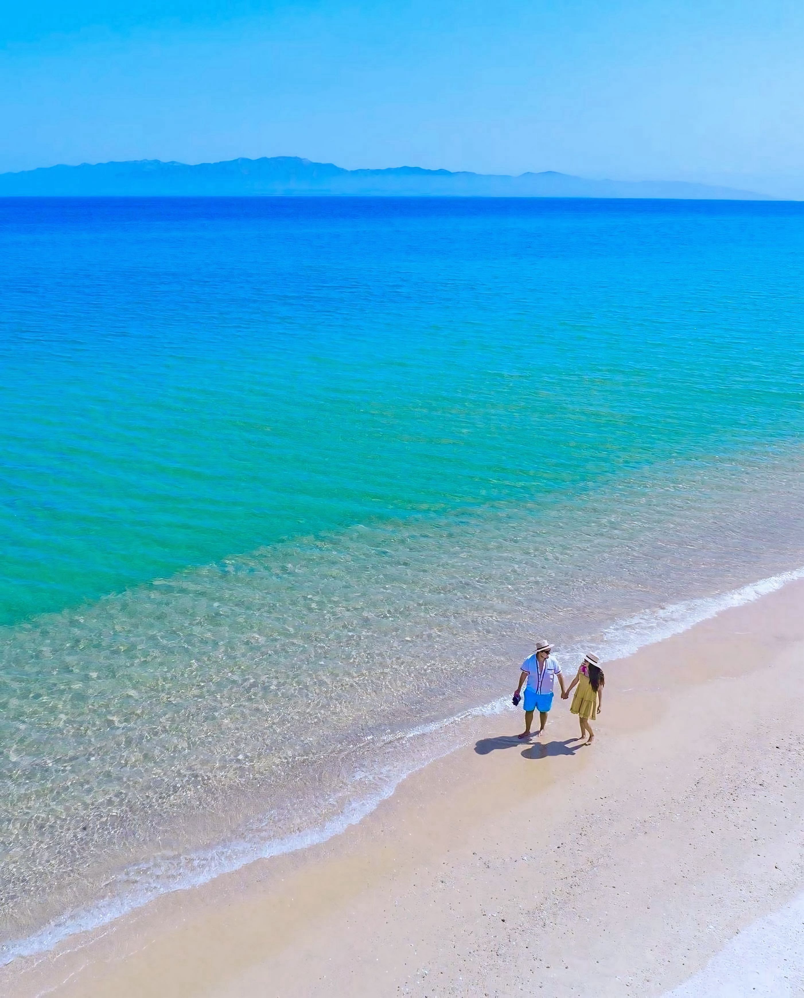 Una playa con agua turquesa cristalina y una cadena montañosa distante.