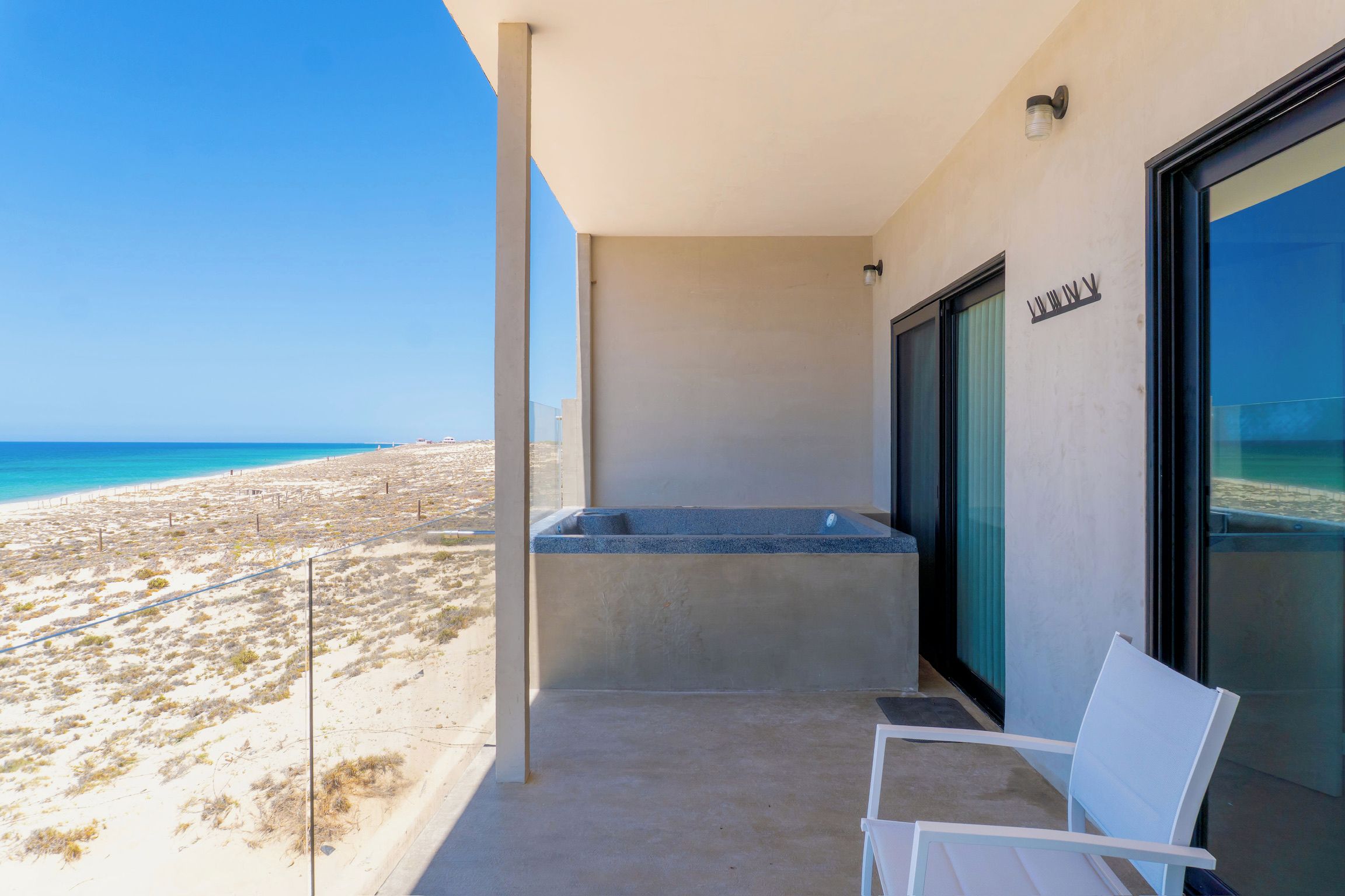 A balcony with a view of the beach, a hot tub, and a seating area.