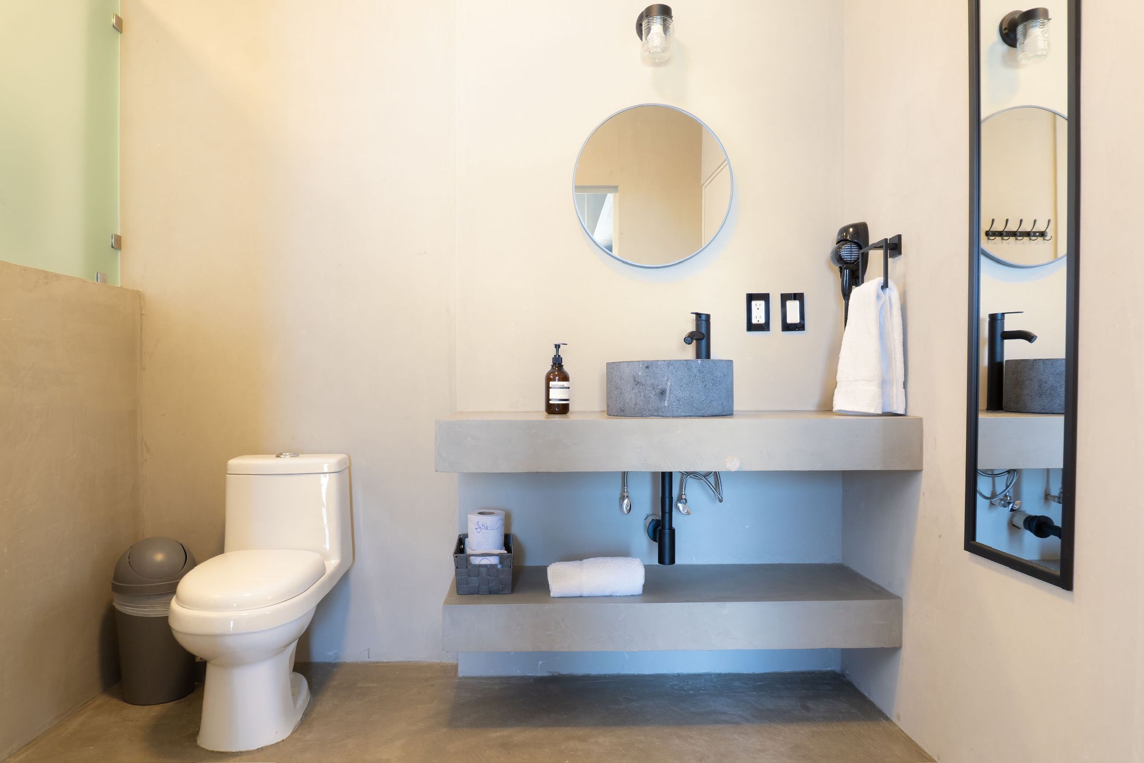 Un baño con inodoro, lavamanos con espejo y un perchero para toallas.