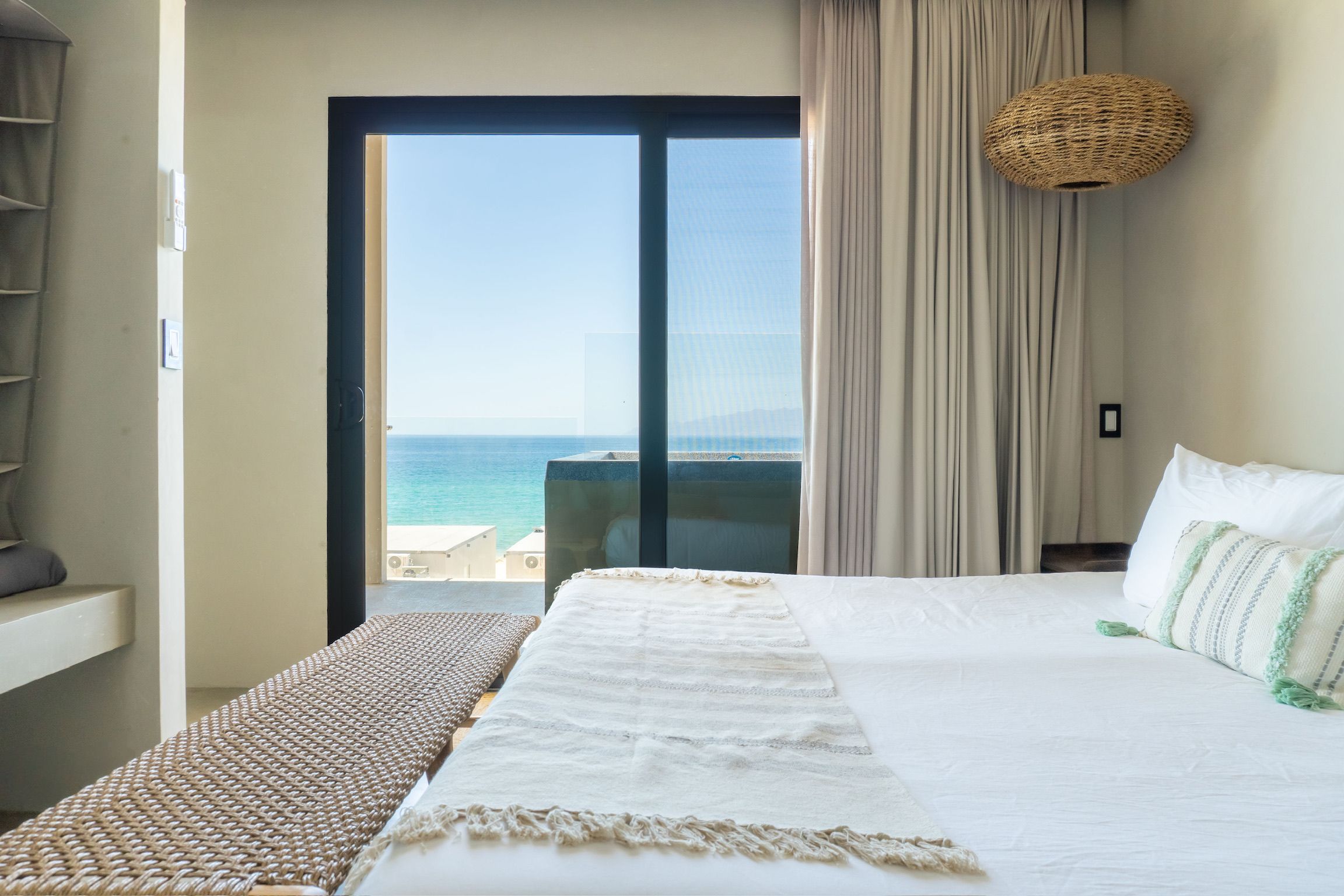 Habitación de hotel con cama, vista al mar, balcón y una lámpara de fibra natural.