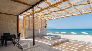 Un espace extérieur aménagé avec des fauteuils confortables et un jacuzzi, offrant une vue sur une plage parsemée de parasols.