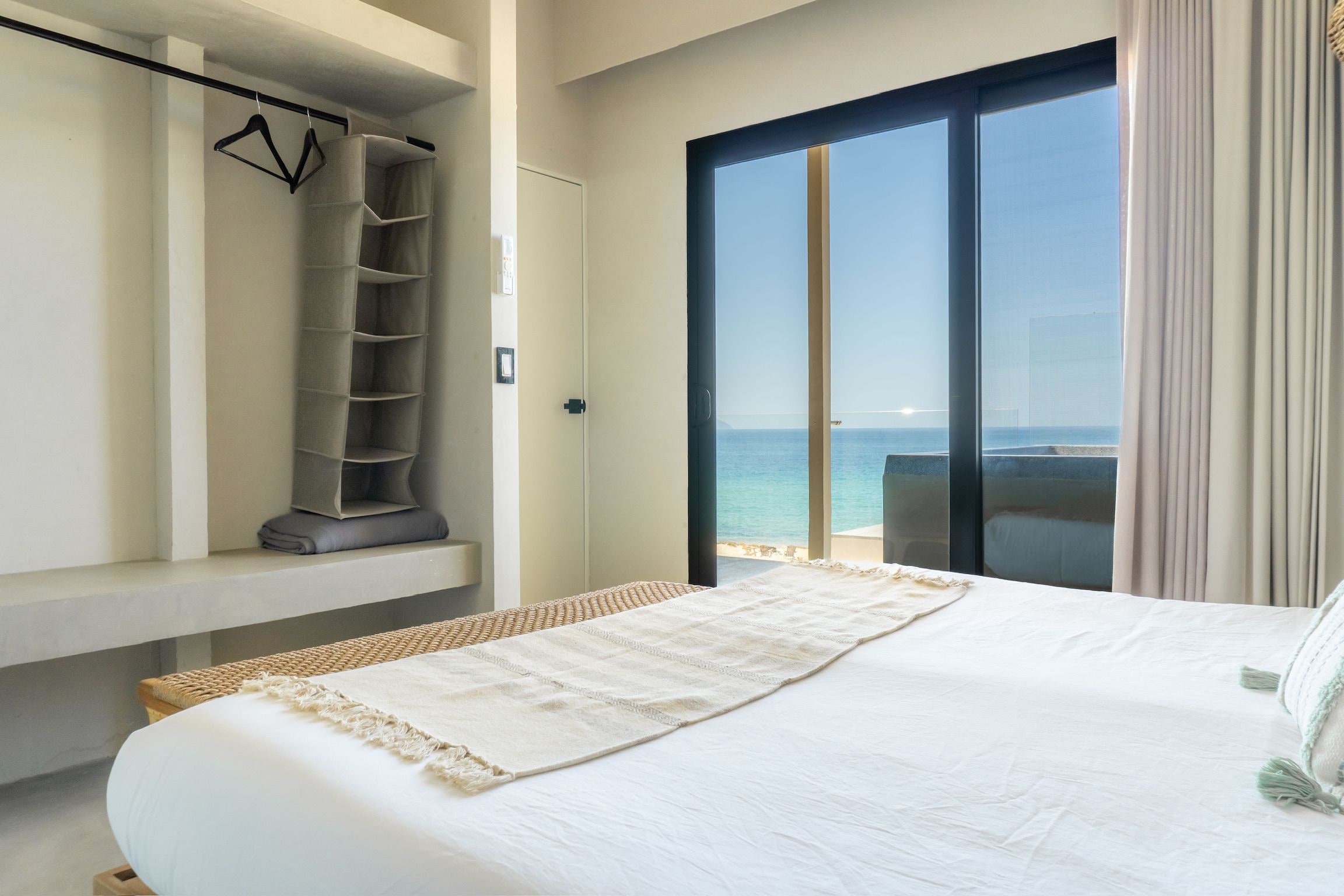 A hotel room with a bed, a built-in wardrobe, a view of the sea, and a balcony.