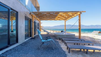 A beachside patio with a wooden pergola, lounge chairs, and a view of the ocean.