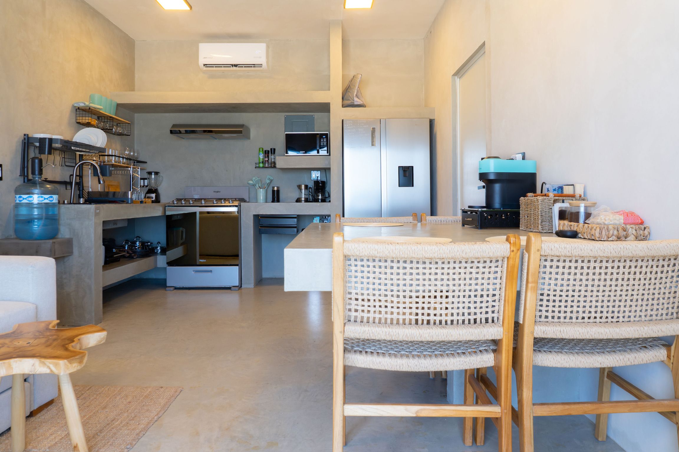 A modern kitchen with a central island, built-in appliances, and a dining area with wicker chairs.