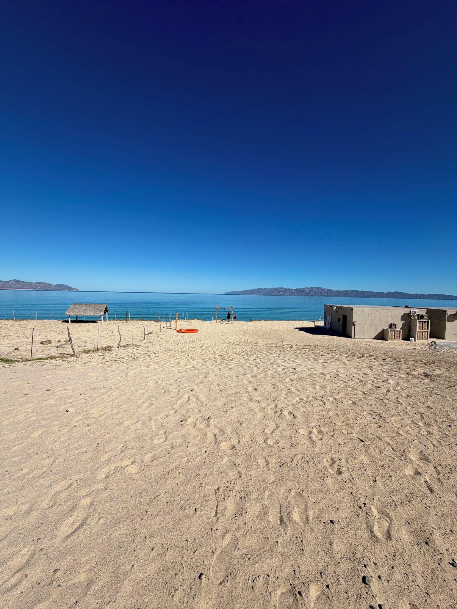 A beach with footprints, a small hut, and a fenced area.