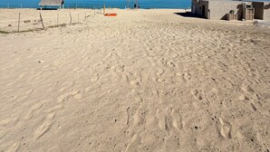 Une plage parsemée d’empreintes, une petite cabane et une zone délimitée par une clôture.