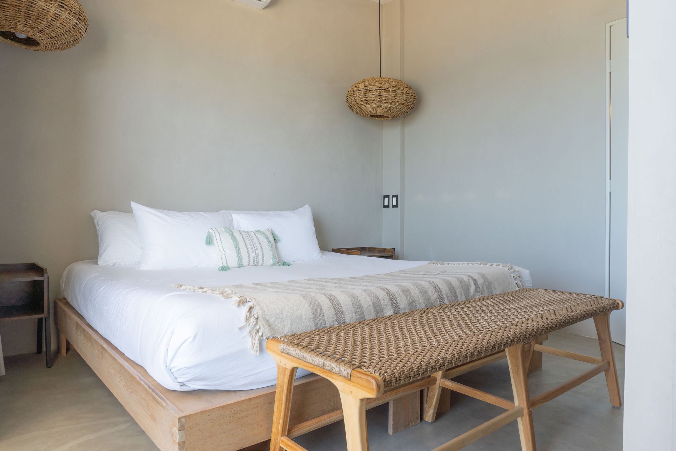 Un dormitorio con una cama de madera, un banco tejido y dos adornos de mimbre en las paredes.