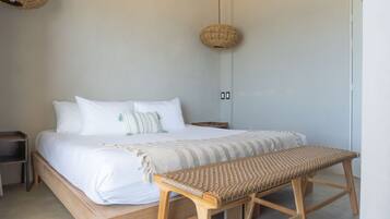 Un dormitorio con una cama de madera, un banco tejido y dos adornos de mimbre en las paredes.