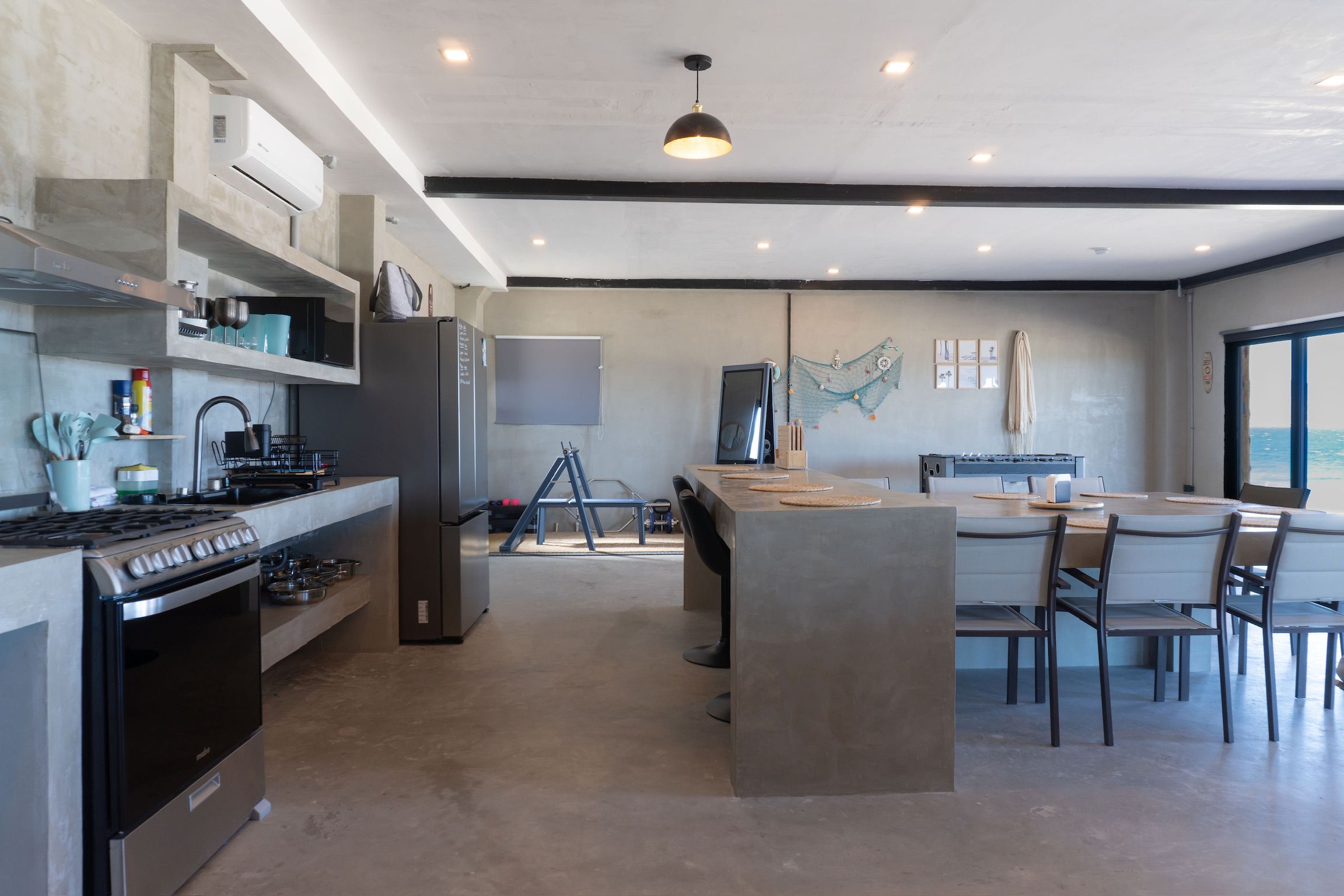 A modern kitchen with a central island, a dining area with chairs, and a large window offering a view.