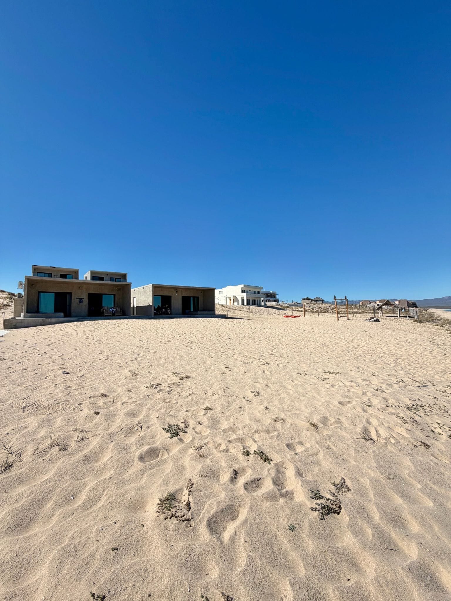 A sandy beach with modern buildings and a clear blue sky.