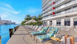 A poolside area with lounge chairs, umbrellas, and a buffet table with food and drinks. - Modern Beachwalk Studio with Resort Amenities (Hallandale Beach)