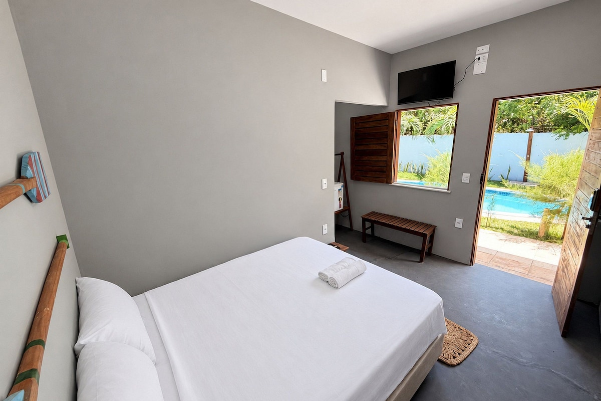 Quarto com cama, um banco, uma TV e vista para uma piscina.