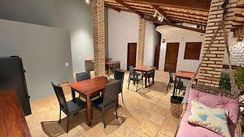 Un área de comedor al aire libre con pilares de ladrillo, mesas de madera y sillas tejidas negras.