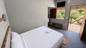 Quarto com cama, um banquinho, televisão e vista para área verde.