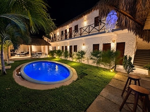 A pool area with a thatched roof, a white building with wooden shutters, and outdoor seating. - Hosts BR - Wind Suites (Barra Grande)